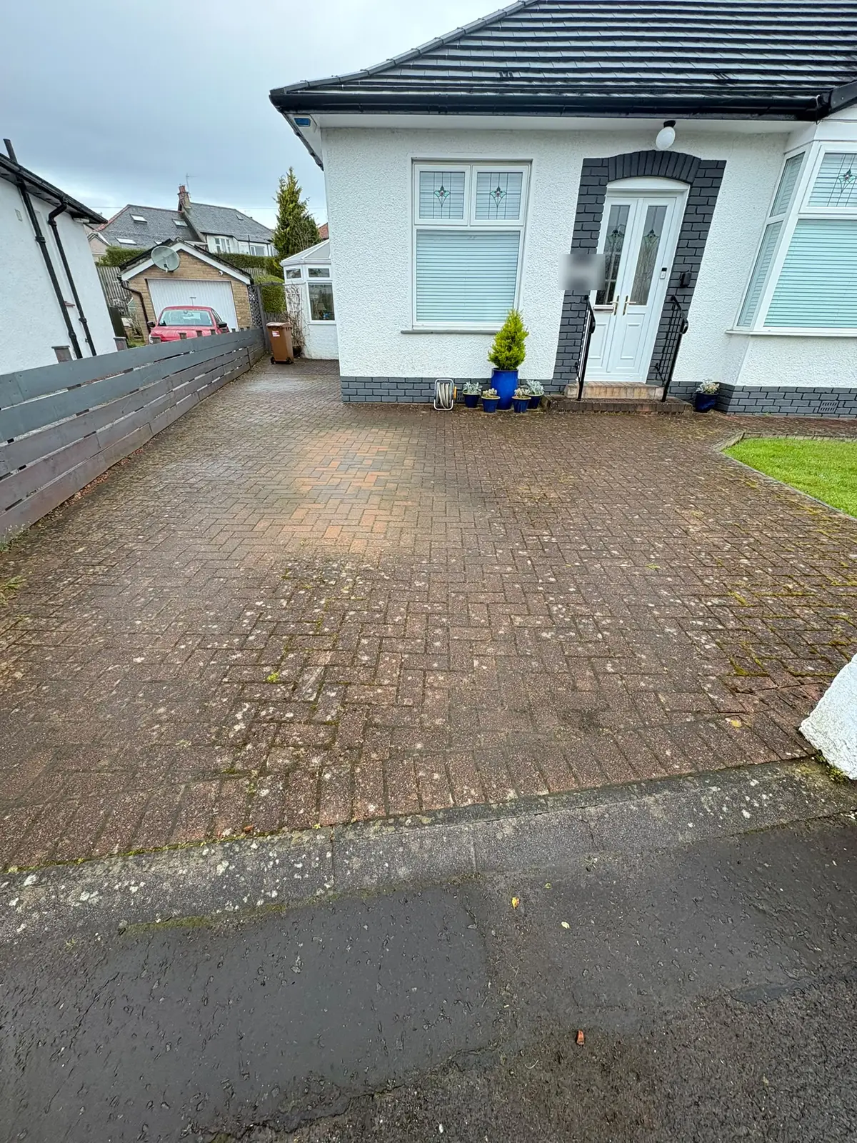A dark, mossy block-paved driveway in front of a white bungalow