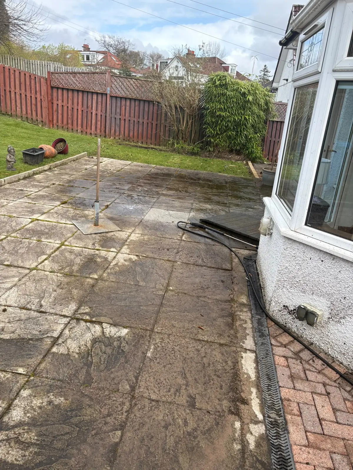 A mossy, stained slab patio beside a conservatory, with a drain channel along the edge