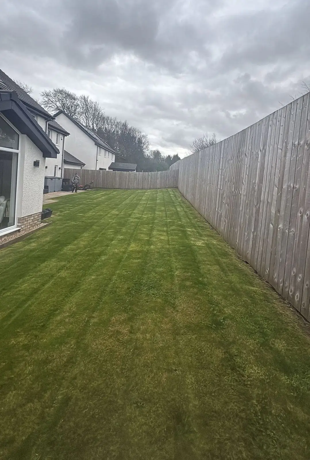 A long striped lawn beside a timber fence at a new-build house