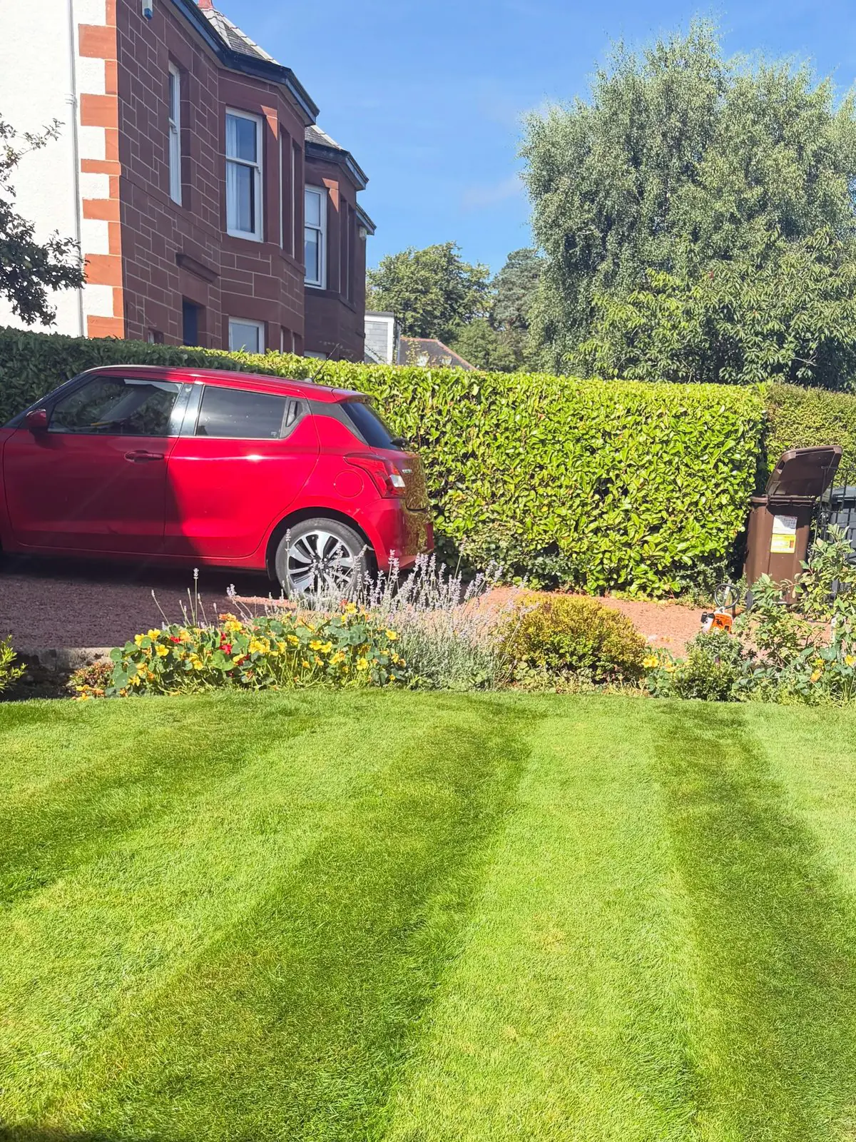 A striped front lawn with clipped hedges in front of a red sandstone villa