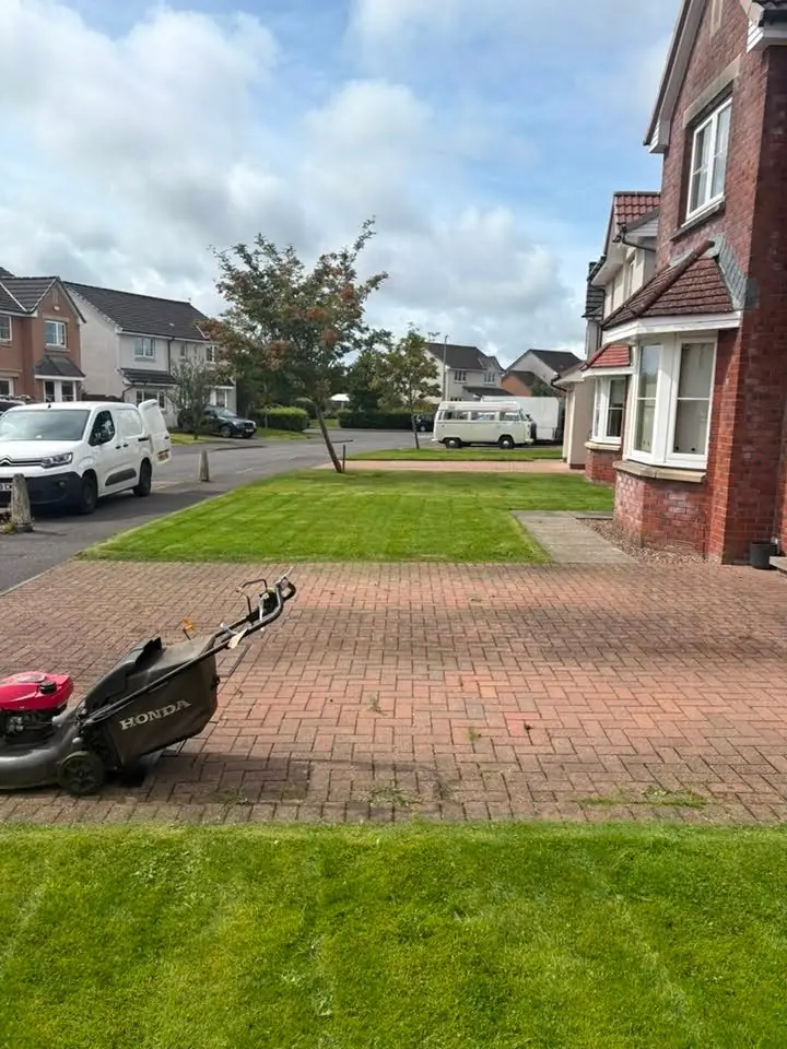 A mower on block paving beside a lawn