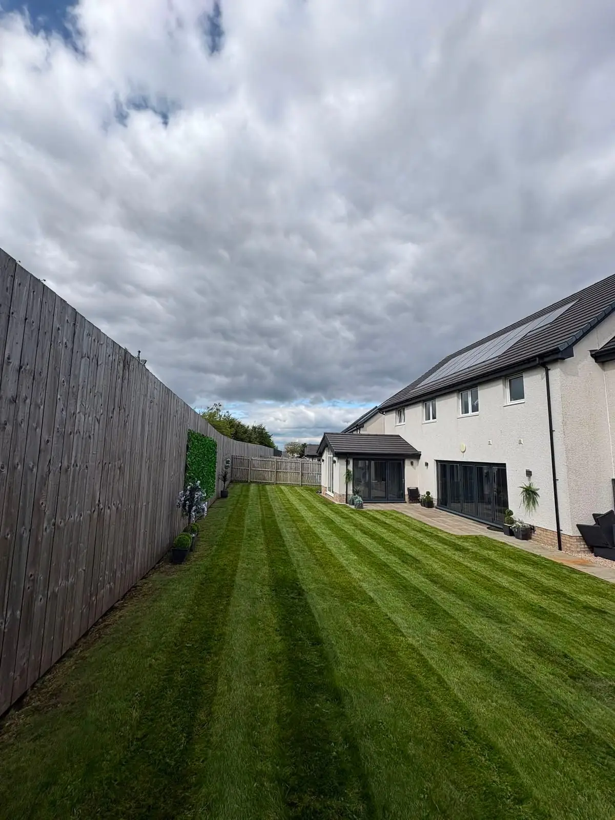 A boldly striped lawn at a new-build house under a cloudy sky